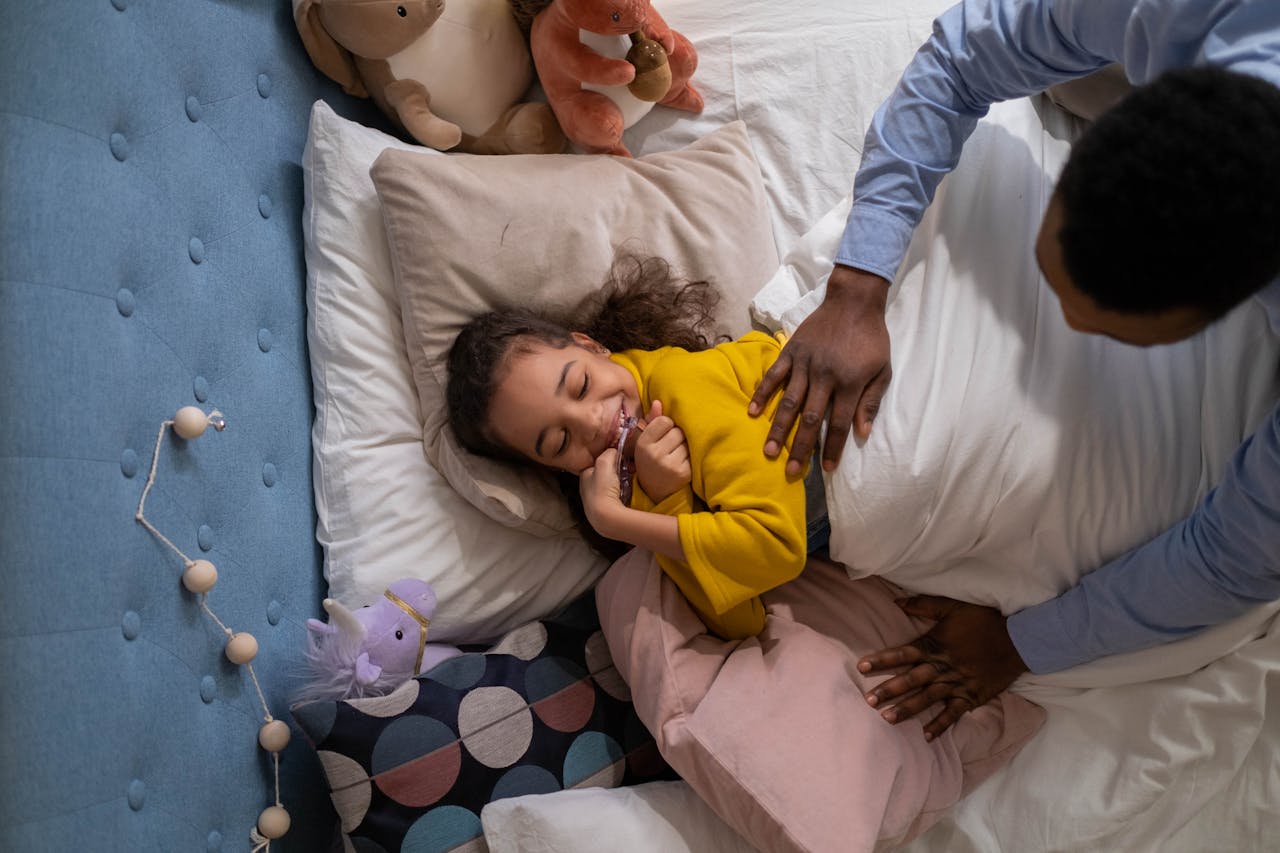 A loving father enjoys playful moments with his daughter tucked in bed with plush toys.